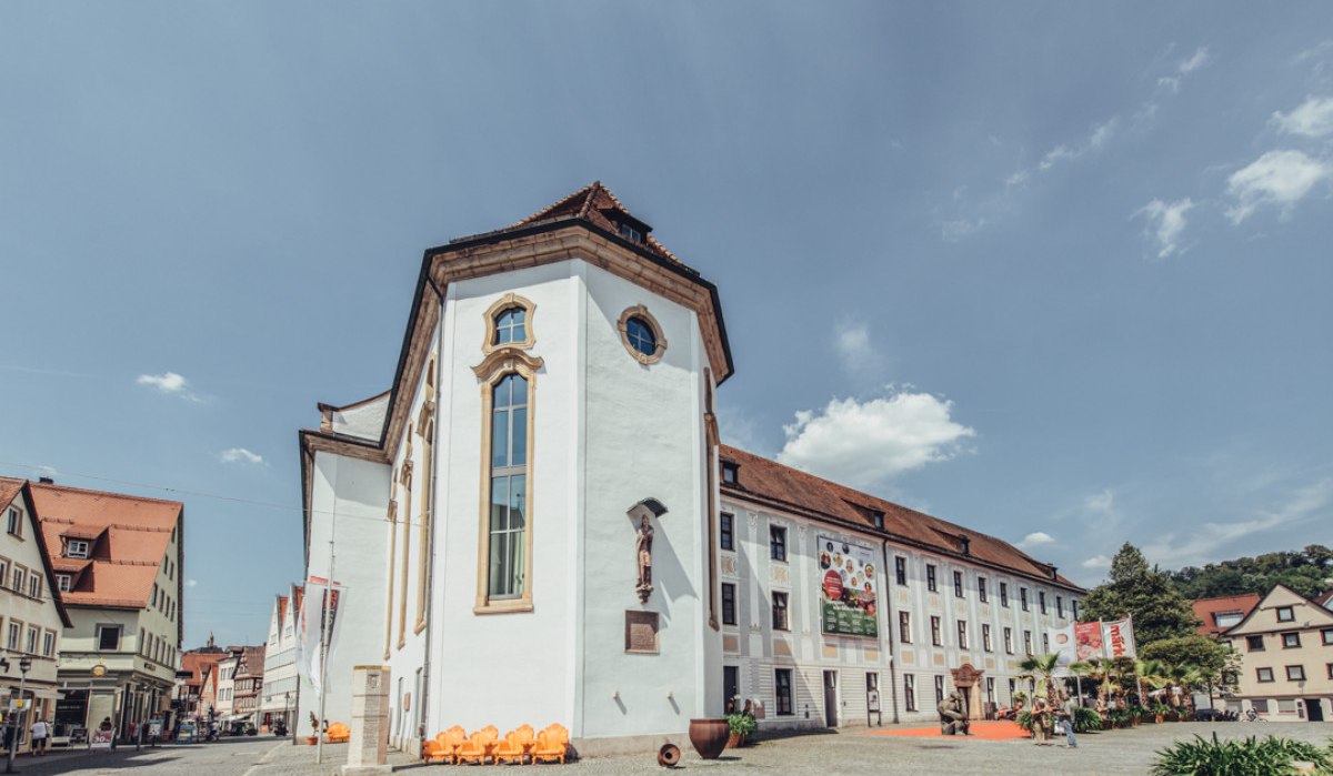 Das Museum im Prediger in Schwäbisch Gmünd, ein historisches Gebäude mit weißen Wänden und roten Dächern, bei sonnigem Wetter. Menschen und Pflanzen im Vordergrund., © Tourismus Ostalb, Fotograf: Christian Frumolt