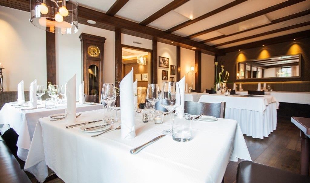 Elegantes Restaurant mit weißen Tischdecken, Gläsern und Besteck. Holzbalkendecke, Wanduhr und Spiegel im Hintergrund. Gemütliche, stilvolle Atmosphäre., © Hotel Waldhorn Elegantes Restaurant mit weißen Tischdecken, Gläsern und Besteck. Holzbalkendecke, Wanduhr und Spiegel im Hintergrund. Gemütliche, stilvolle Atmosphäre., © Hotel Waldhorn