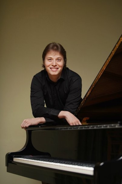 Eine Person in schwarzem Hemd lehnt sich lächelnd auf einen Flügel. Der Hintergrund ist schlicht und hell., © Stadt Böblingen - Amt für Kultur