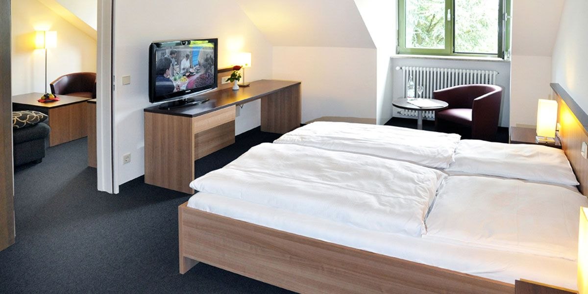 Modernes Doppelzimmer mit Doppelbett, Schreibtisch, Fernseher und Sitzbereich. Helle Einrichtung und Fenster mit Blick ins Grüne., © Christkönigshaus Modernes Doppelzimmer mit Doppelbett, Schreibtisch, Fernseher und Sitzbereich. Helle Einrichtung und Fenster mit Blick ins Grüne., © Christkönigshaus