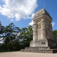 Ein massiver Bismarckturm aus Stein steht auf einem Platz, umgeben von Bäumen und unter einem blauen Himmel mit wenigen Wolken., © SMG Ein massiver Bismarckturm aus Stein steht auf einem Platz, umgeben von Bäumen und unter einem blauen Himmel mit wenigen Wolken., © SMG