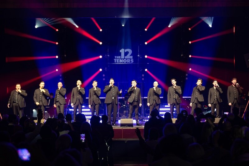 Zwölf Tenöre stehen auf einer Bühne, singen in Mikrofone. Bunte Lichteffekte und ein Publikum im Vordergrund. Schriftzug 'The 12 Tenors' im Hintergrund., © die Halle Kulturinitiative e.V. Zwölf Tenöre stehen auf einer Bühne, singen in Mikrofone. Bunte Lichteffekte und ein Publikum im Vordergrund. Schriftzug 'The 12 Tenors' im Hintergrund., © die Halle Kulturinitiative e.V.