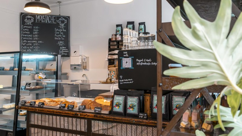 Ein gem&uuml;tliches Caf&eacute; mit Theke, Geb&auml;ckauslage und Getr&auml;nkekarte. Pflanzen schm&uuml;cken den Raum, und eine Tafel zeigt das Men&uuml; an., &copy; SMG, Sarah Schmid