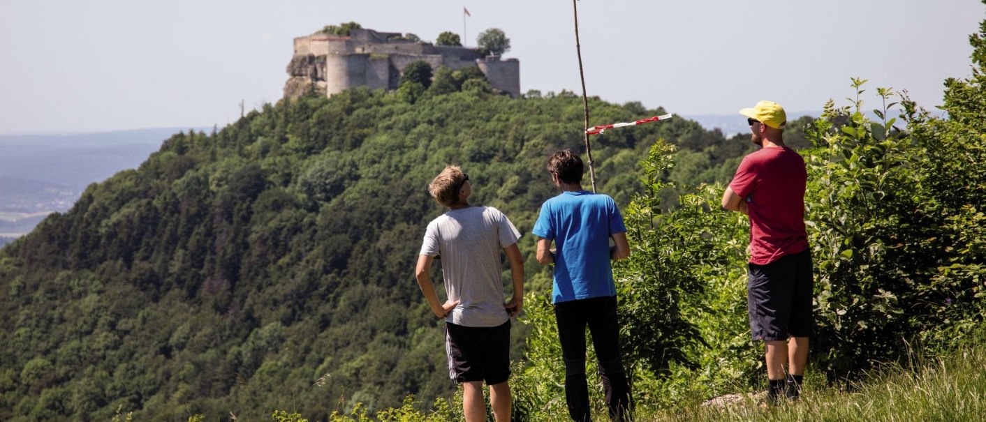 Drei Personen stehen auf einem Hügel und blicken auf die Ruine Hohenneuffen, die von Bäumen umgeben ist., © Stuttgart-Marketing GmbH Achim Mende