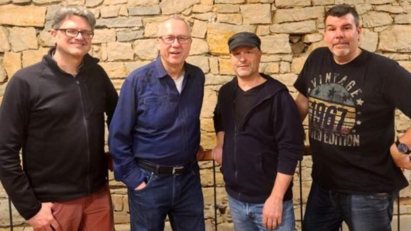 Vier M&auml;nner posieren l&auml;chelnd vor einer Steinmauer. Sie tragen l&auml;ssige Kleidung und wirken entspannt., &copy; Foto Uli Binetsch