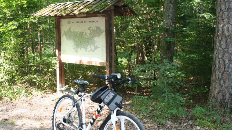 Ein Fahrrad steht vor einer Infotafel mit Karte des Naturparks Schönbuch, umgeben von dichtem Wald., © Natur.Nah. Schönbuch & Heckengäu