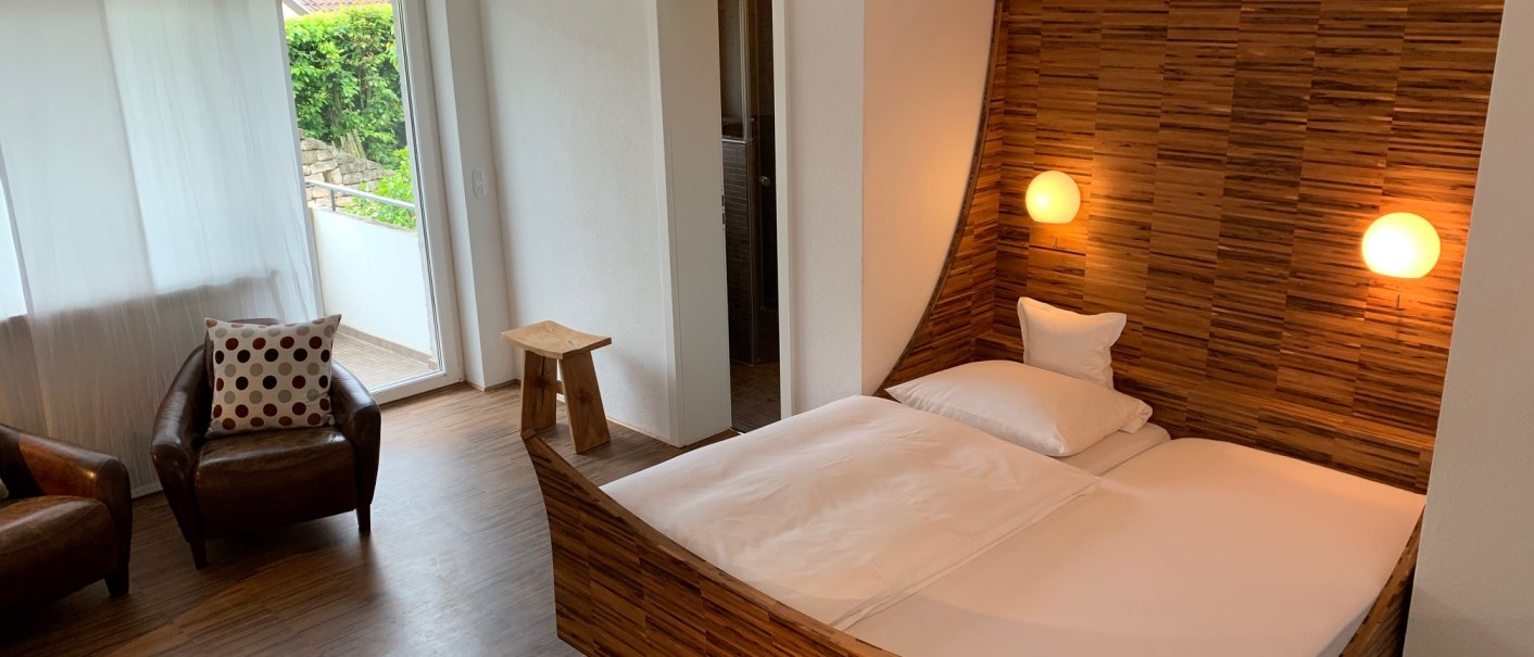 Modernes Schlafzimmer mit Holzdekor, Doppelbett, zwei Sesseln und Zugang zu einem kleinen Balkon., © TOMAS