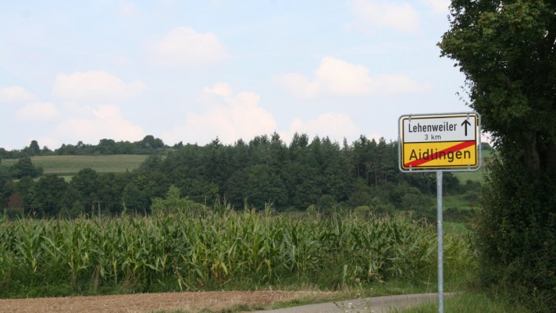 Straßenschild zeigt das Ende von Aidlingen und Richtung nach Lehenweiler. Umgebung mit Feldern und Bäumen, blauer Himmel im Hintergrund., © Natur.Nah. Schönbuch & Heckengäu Straßenschild zeigt das Ende von Aidlingen und Richtung nach Lehenweiler. Umgebung mit Feldern und Bäumen, blauer Himmel im Hintergrund., © Natur.Nah. Schönbuch & Heckengäu
