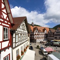 Blick auf den Marktplatz in Bad Urach mit malerischen Fachwerkhäusern und bunten Marktständen unter einem blauen Himmel mit Wolken., © Bad Urach Tourismus Blick auf den Marktplatz in Bad Urach mit malerischen Fachwerkhäusern und bunten Marktständen unter einem blauen Himmel mit Wolken., © Bad Urach Tourismus