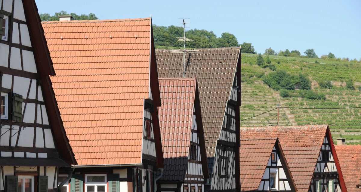 Fachwerkhäuser mit roten Ziegeldächern in Roßwag, im Hintergrund grüne Weinberge unter blauem Himmel., © Land der 1000 Hügel - Kraichgau-Stromberg