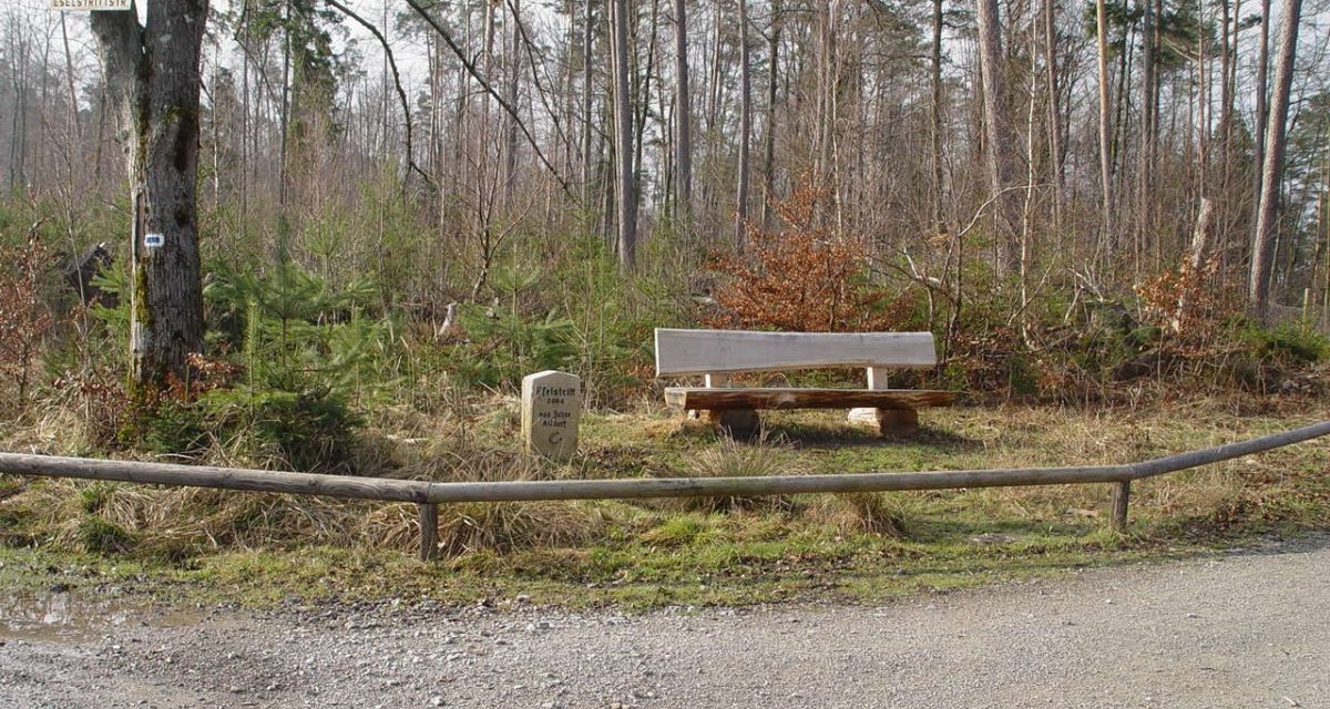 Eine Holzbank steht im Wald neben einem Gedenkstein und einem Wegweiser. Der Boden ist mit Kies bedeckt, und B&auml;ume umgeben die Szene., &copy; Naturpark Sch&ouml;nbuch