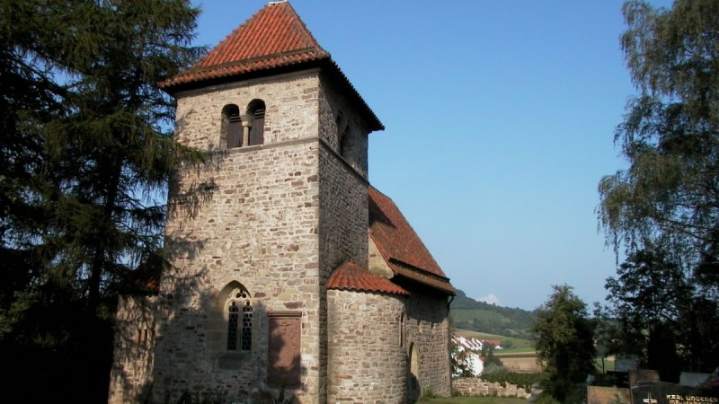 Romanische Kirche mit rotem Ziegeldach und Glockenturm, umgeben von Bäumen und Landschaft. Der Himmel ist klar und blau., © Tourismusgemeinschaft Marbach-Bottwartal