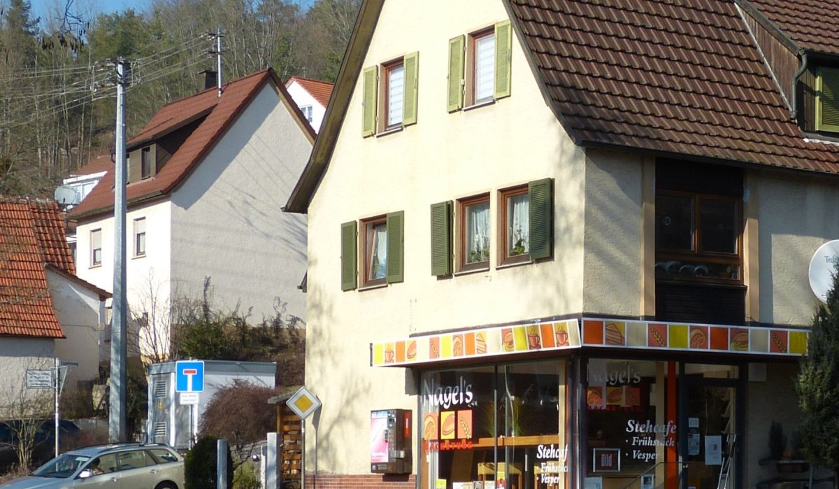 Ein Stehcafé in einem Eckgebäude mit gelber Fassade und grünen Fensterläden in Dätzingen. Im Hintergrund sind weitere Häuser und Bäume zu sehen., © Natur.Nah. Schönbuch & Heckengäu