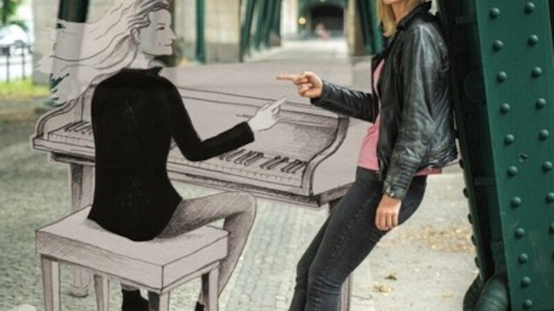Eine Frau lehnt an einem Brückenpfeiler und zeigt auf eine gezeichnete Person, die Klavier spielt. Die Szene ist unter einer Brücke., © Mauerwerk GmbH Eine Frau lehnt an einem Brückenpfeiler und zeigt auf eine gezeichnete Person, die Klavier spielt. Die Szene ist unter einer Brücke., © Mauerwerk GmbH