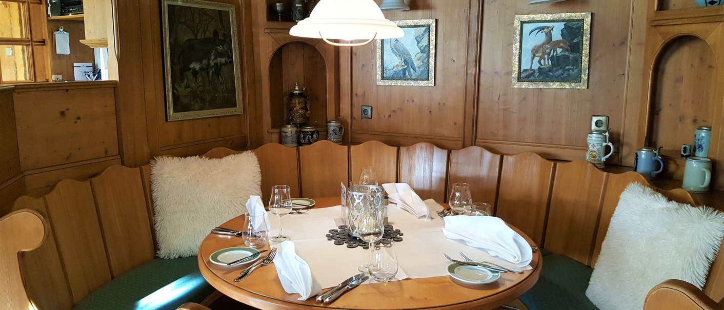Gemütliche Sitzecke mit Holzwänden, rundem Tisch, weißen Kissen und dekorativen Bildern. Geschirr und Gläser sind auf dem Tisch arrangiert., © Erikson Hotel Sindelfingen