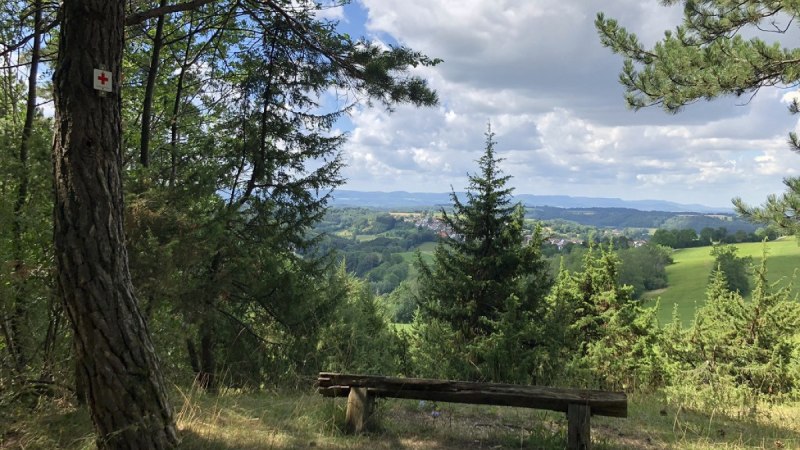 Holzbank unter B&auml;umen mit Blick auf Wi&szlig;goldingen. Gr&uuml;ne H&uuml;gel und bew&ouml;lkter Himmel im Hintergrund., &copy; Touristik und Marketing GmbH