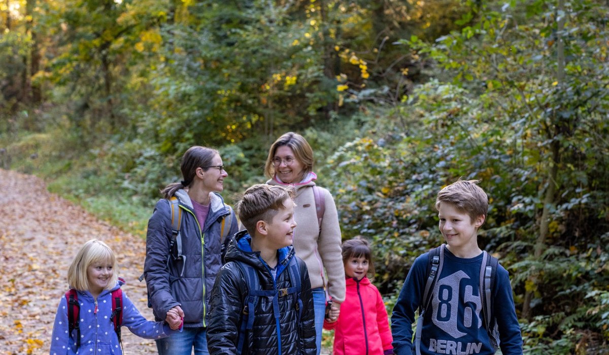 Eine Familie wandert auf einem Waldweg im Herbst. Die Erwachsenen und Kinder tragen Jacken und Rucksäcke. Der Boden ist mit Laub bedeckt., © Fotograf Thomas Zehnder