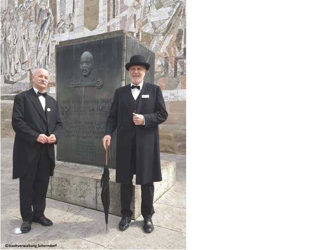 Zwei Männer in historischer Kleidung posieren vor einem Gottlieb-Daimler-Denkmal in Schorndorf. Sie tragen Anzüge und Hüte und halten Regenschirme., © Eigenbetrieb Tourismus und Citymanagement Schorndorf Zwei Männer in historischer Kleidung posieren vor einem Gottlieb-Daimler-Denkmal in Schorndorf. Sie tragen Anzüge und Hüte und halten Regenschirme., © Eigenbetrieb Tourismus und Citymanagement Schorndorf