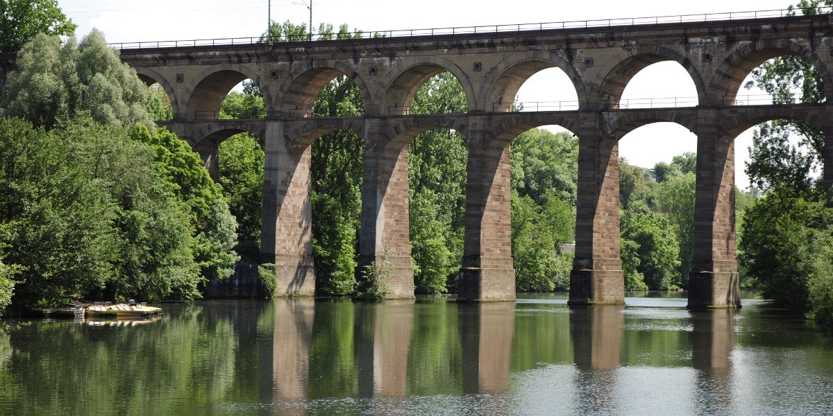 Ein Viadukt in Bietigheim-Bissingen spannt sich über einen Fluss, umgeben von üppigem Grün und Bäumen, die sich im Wasser spiegeln., © Stuttgart-Marketing GmbH Ein Viadukt in Bietigheim-Bissingen spannt sich über einen Fluss, umgeben von üppigem Grün und Bäumen, die sich im Wasser spiegeln., © Stuttgart-Marketing GmbH
