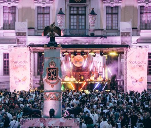 Ein lebhaftes Musikfestival mit einer gro&szlig;en Menschenmenge vor einer B&uuml;hne, die mit Lichteffekten und Bannern mit der Aufschrift 'Melodic Wine' dekoriert ist., &copy; wisio-media GmbH