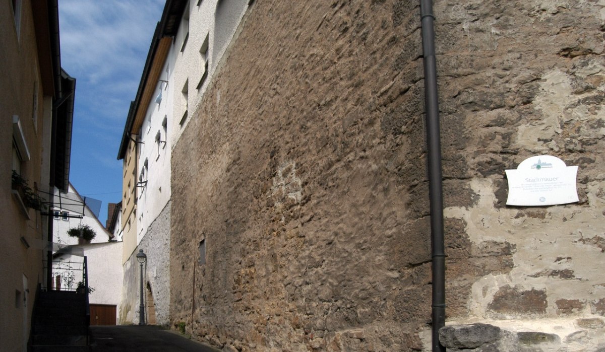 Schmale Gasse zwischen alten Gebäuden, rechts eine historische Stadtmauer mit Schild. Blauer Himmel im Hintergrund., © Natur.Nah. Schönbuch & Heckengäu Schmale Gasse zwischen alten Gebäuden, rechts eine historische Stadtmauer mit Schild. Blauer Himmel im Hintergrund., © Natur.Nah. Schönbuch & Heckengäu