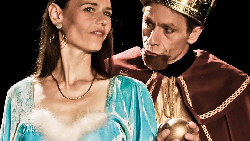 Eine Frau in einem blauen Kleid steht neben einem Mann in k&ouml;niglichem Gewand mit Krone, der eine goldene Kugel h&auml;lt. Beide tragen Kronen., &copy; Galli Theater Backnang