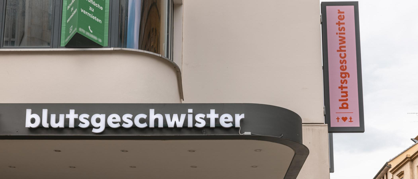 Ein Geschäftsschild mit der Aufschrift 'blutsgeschwister' an einem Gebäude. Ein weiteres Schild zeigt das Logo mit Herz und Anker., © Stuttgart-Marketing GmbH, Sarah Schmid