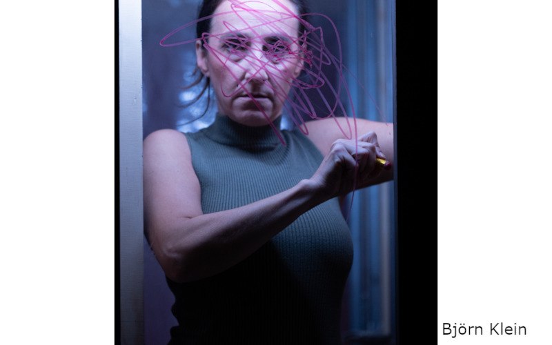 Eine Frau in einem dunklen Raum zeichnet mit einem Stift auf eine Glasscheibe. Die Szene ist in bläulichem Licht gehalten., © Kultur- und Sportamt Stadt Bietigheim-Bissingen