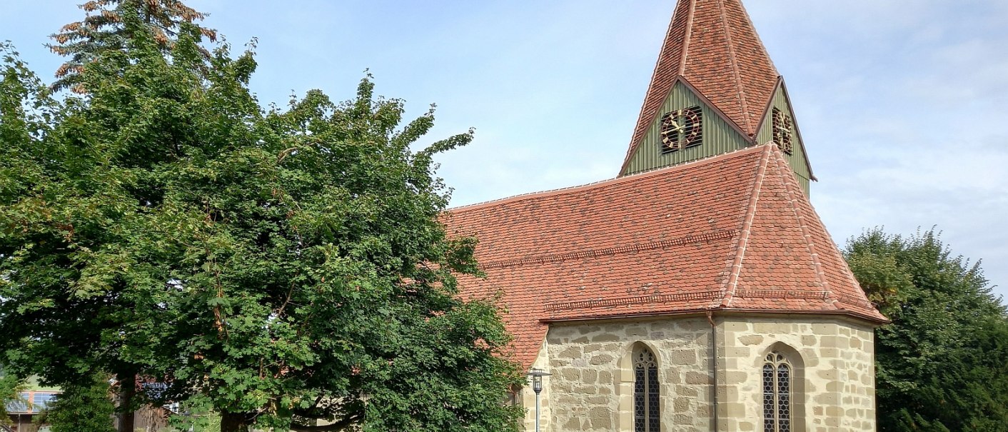 Kirche mit einem  roten Ziegeldach und kleinem Kirchturm, umgeben von gr&uuml;nen B&auml;umen und einem blauen Himmel im Hintergrund., &copy; Petra Natzkowski