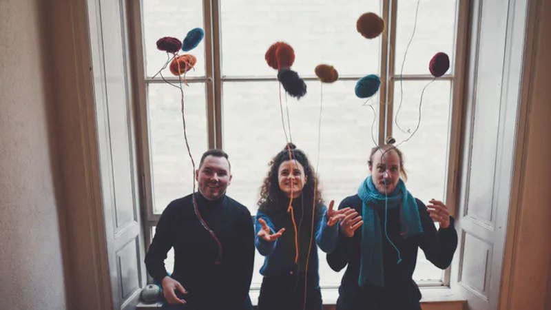 Drei Personen sitzen vor einem großen Fenster und werfen bunte, wollartige Bälle in die Luft. Sie wirken fröhlich und entspannt., © Jazzclub Schwäbisch Hall e.V.