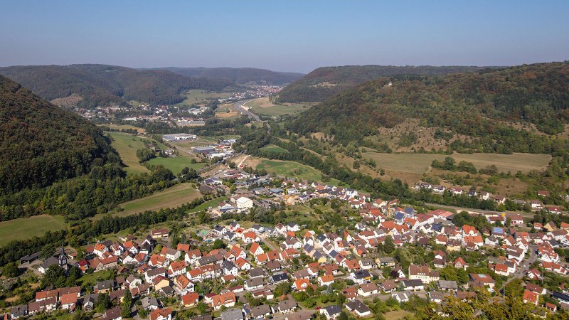 Luftaufnahme von Bad Diutzenbach, umgeben von grünen Hügeln und Wäldern. Im Vordergrund sind Häuser und Straßen zu sehen, im Hintergrund erstreckt sich die Landschaft., © Stuttgart-Marketing GmbH / Achim Mende