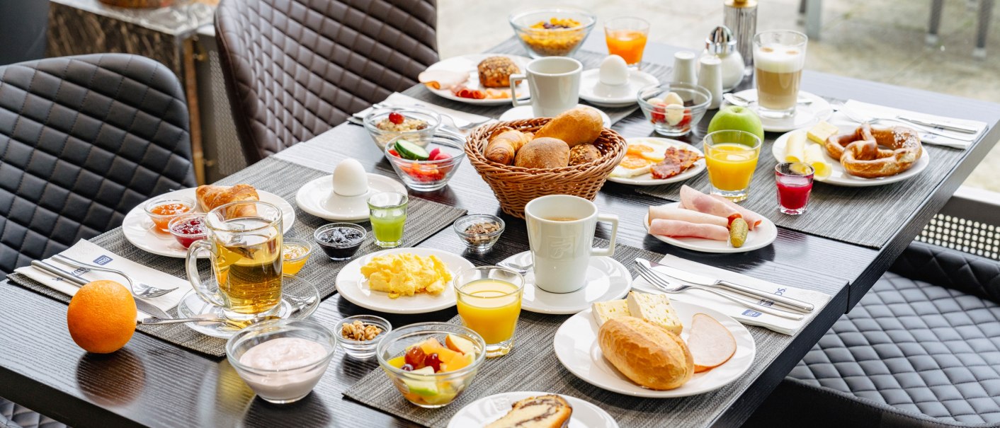 Ein reich gedeckter Frühstückstisch mit Brötchen, Eiern, Aufschnitt, Obst, Saft und Kaffee. Verschiedene Speisen sind auf weißen Tellern angerichtet., © Plaza Residence Stuttgart-Ditzingen Ein reich gedeckter Frühstückstisch mit Brötchen, Eiern, Aufschnitt, Obst, Saft und Kaffee. Verschiedene Speisen sind auf weißen Tellern angerichtet., © Plaza Residence Stuttgart-Ditzingen