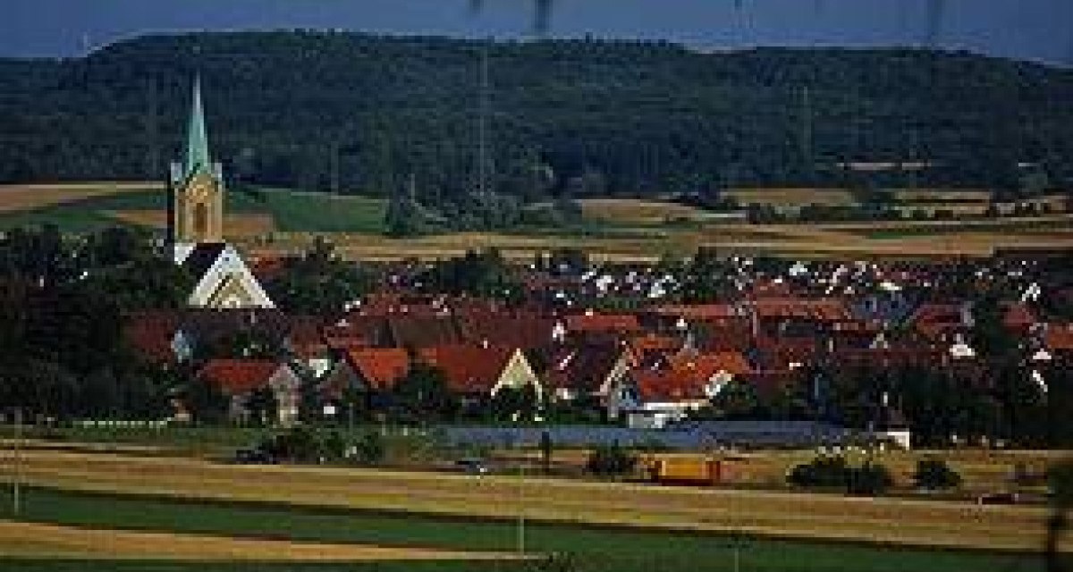 Ein Dorf mit roten Dächern und einer Kirche mit grünem Turm, umgeben von Feldern und Hügeln im Hintergrund., © http://www.renningen.de/index.php?id=574
