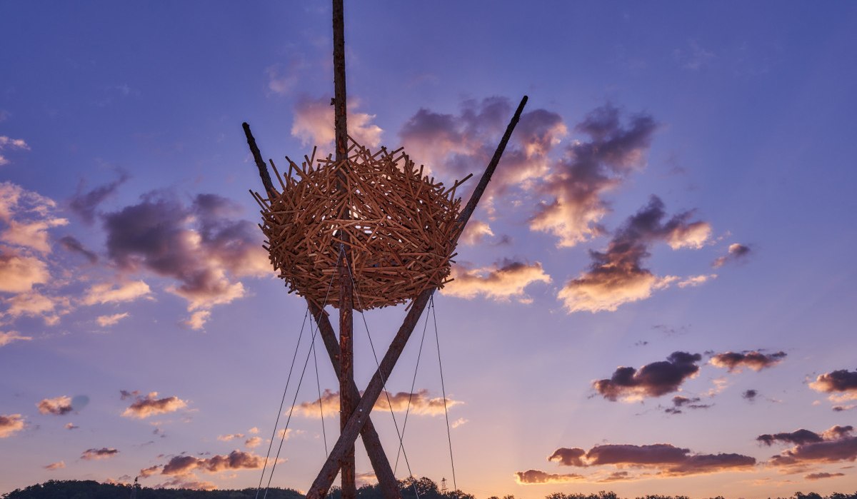 Eine große Vogelnest-Skulptur aus Holz thront vor einem dramatischen Sonnenuntergang mit violettem Himmel und Wolken., © Natur.Nah. Schönbuch & Heckengäu Eine große Vogelnest-Skulptur aus Holz thront vor einem dramatischen Sonnenuntergang mit violettem Himmel und Wolken., © Natur.Nah. Schönbuch & Heckengäu