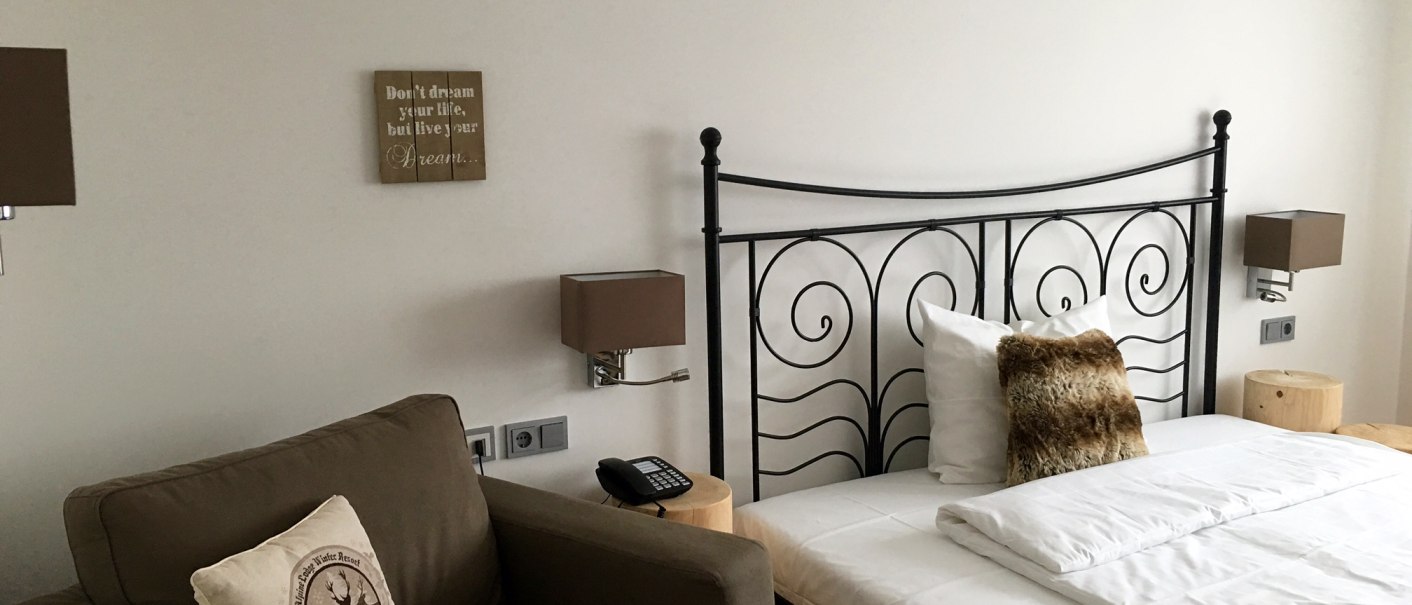 Modernes Schlafzimmer mit Metallbett, braunem Sessel und dekorativen Kissen. An der Wand hängen motivierende Sprüche., © TOMAS Modernes Schlafzimmer mit Metallbett, braunem Sessel und dekorativen Kissen. An der Wand hängen motivierende Sprüche., © TOMAS