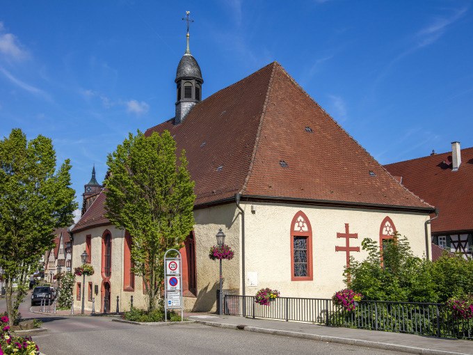 Eine historische Kirche mit rotem Dach und kleinem Glockenturm, umgeben von B&auml;umen und Blumen, unter blauem Himmel., &copy; Stadtverwaltung Weil der Stadt