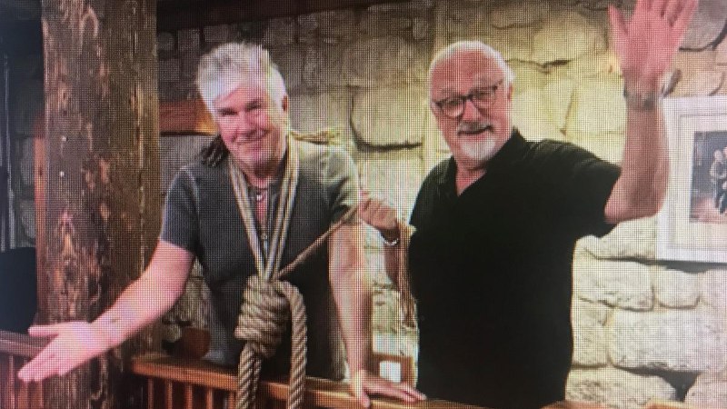 Zwei Männer stehen in einem rustikalen Raum. Einer hat ein Seil um den Hals, beide lächeln und gestikulieren freundlich., © Kabarett der Galgenstricke Zwei Männer stehen in einem rustikalen Raum. Einer hat ein Seil um den Hals, beide lächeln und gestikulieren freundlich., © Kabarett der Galgenstricke