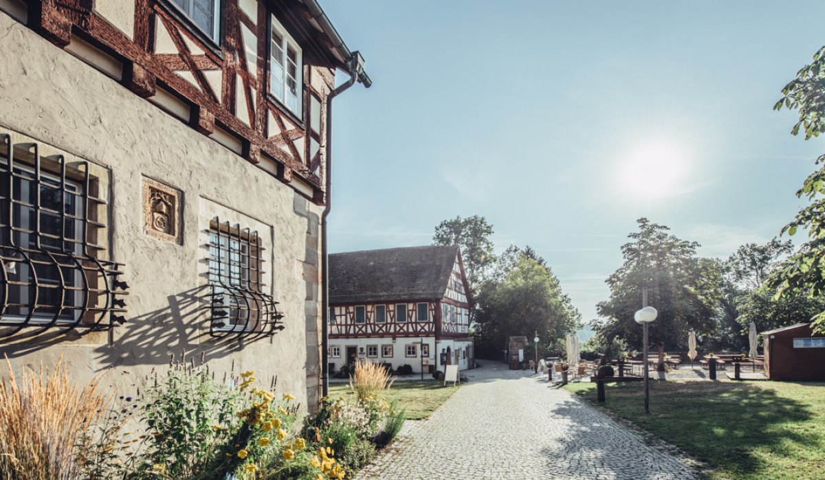 Innenhof des Klosters Lorch mit Fachwerkgebäuden, gepflastertem Weg und blühenden Pflanzen bei sonnigem Wetter., © Tourismus Ostalb