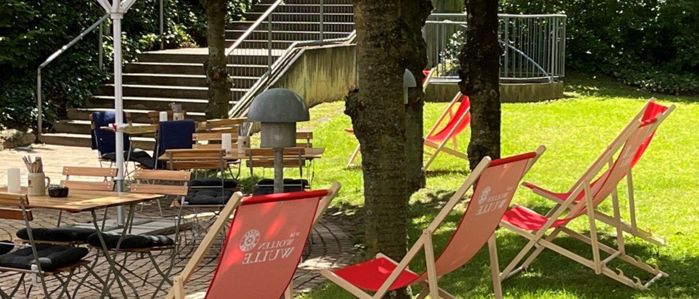 Ein Garten mit roten Liegestühlen und Holztischen unter weißen Sonnenschirmen, umgeben von Bäumen und einer Treppe im Hintergrund., © Holiday Inn Stuttgart Ein Garten mit roten Liegestühlen und Holztischen unter weißen Sonnenschirmen, umgeben von Bäumen und einer Treppe im Hintergrund., © Holiday Inn Stuttgart