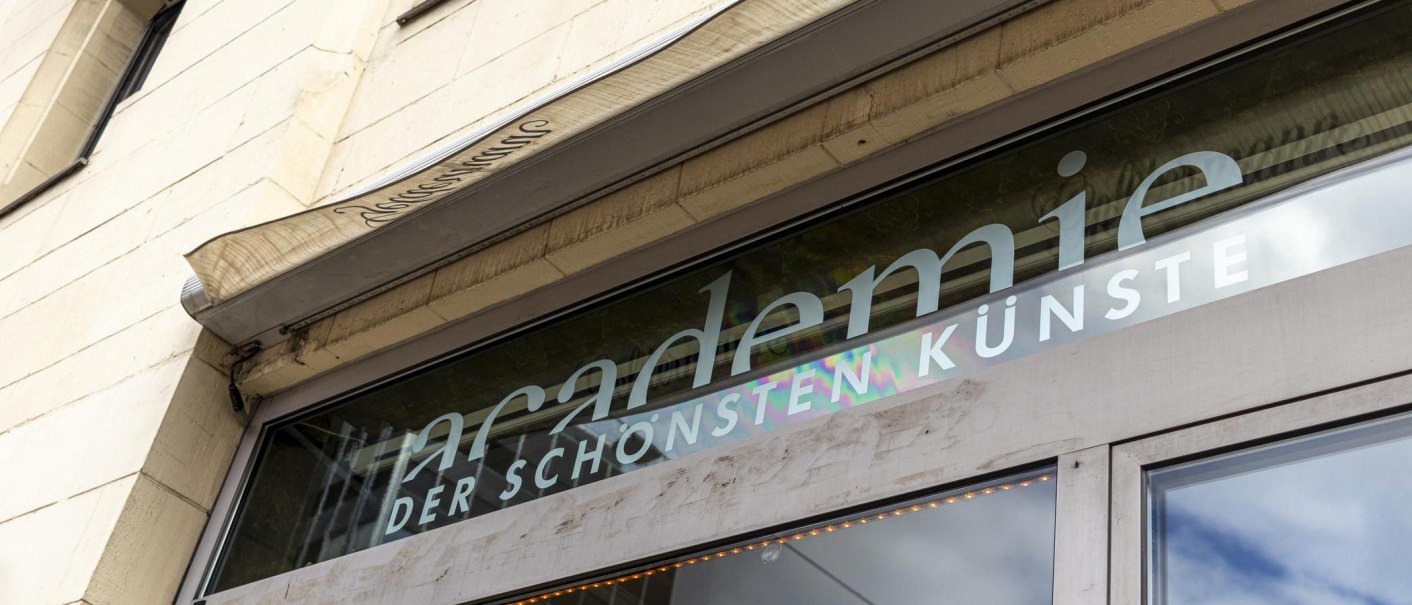 Nahaufnahme des Eingangs der Akademie der schönsten Künste mit Schriftzug auf einer Glasfront., © SMG, Sarah Schmid