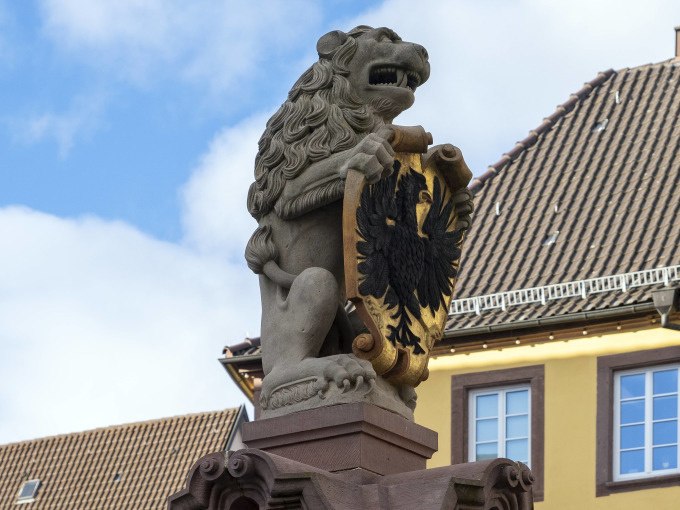 Ein steinerner Löwe hält ein Wappen mit einem Adler. Im Hintergrund ist ein Gebäude mit Ziegeldach zu sehen., © Stadtverwaltung Weil der Stadt Ein steinerner Löwe hält ein Wappen mit einem Adler. Im Hintergrund ist ein Gebäude mit Ziegeldach zu sehen., © Stadtverwaltung Weil der Stadt