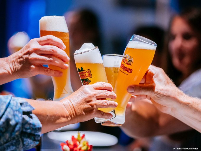 Mehrere Personen sto&szlig;en mit gef&uuml;llten Biergl&auml;sern an, im Hintergrund sind unscharfe Gesichter zu sehen., &copy; Stuttgart Marketing GmbH