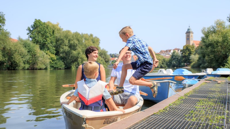 Eine Familie sitzt in einem Ruderboot auf dem Neckar. Ein Junge springt ins Boot. Im Hintergrund sind B&auml;ume und ein Kirchturm zu sehen., &copy; H. Bergm&uuml;ller
