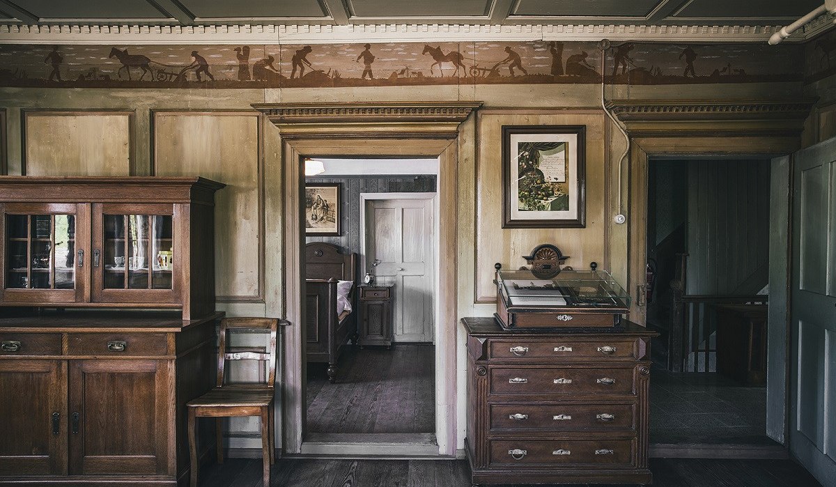 Historischer Raum mit Holzmöbeln, Wandmalereien und antiken Dekorationen. Ein Schrank, eine Kommode und ein Durchgang zu einem weiteren Raum sind sichtbar., © Unbekannt Historischer Raum mit Holzmöbeln, Wandmalereien und antiken Dekorationen. Ein Schrank, eine Kommode und ein Durchgang zu einem weiteren Raum sind sichtbar., © Unbekannt