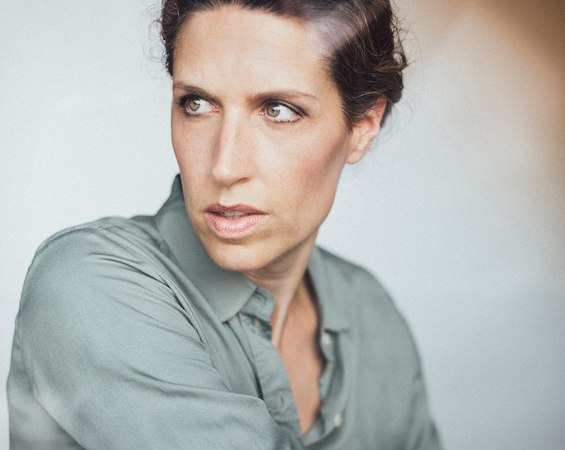 Frau in grauem Hemd blickt nach links, mit ernstem Gesichtsausdruck. Der Hintergrund ist unscharf, was den Fokus auf ihr Gesicht lenkt., © Scala Kultur Live gGmbH Frau in grauem Hemd blickt nach links, mit ernstem Gesichtsausdruck. Der Hintergrund ist unscharf, was den Fokus auf ihr Gesicht lenkt., © Scala Kultur Live gGmbH