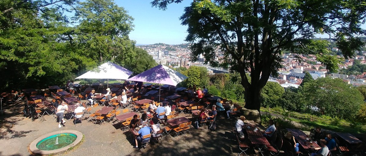 Ein Biergarten auf der Karlshöhe mit Tischen und Sonnenschirmen, umgeben von Bäumen. Im Hintergrund ist die Stadt Stuttgart zu sehen., © Stuttgart-Marketing GmbH Ein Biergarten auf der Karlshöhe mit Tischen und Sonnenschirmen, umgeben von Bäumen. Im Hintergrund ist die Stadt Stuttgart zu sehen., © Stuttgart-Marketing GmbH
