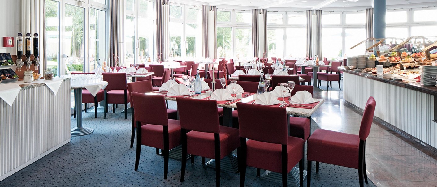 Elegantes Buffet-Restaurant mit roten Stühlen, gedeckten Tischen und großen Fenstern. Ein Buffet mit Speisen ist rechts zu sehen., © Seminaris Hotel Bad Boll Elegantes Buffet-Restaurant mit roten Stühlen, gedeckten Tischen und großen Fenstern. Ein Buffet mit Speisen ist rechts zu sehen., © Seminaris Hotel Bad Boll