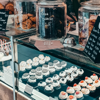 Eine Vitrine in einem Caf&eacute; zeigt eine Auswahl an Cupcakes, Cake Pops und Geb&auml;ck. Daneben stehen Gl&auml;ser mit Keksen und Preisschilder., &copy; Cupcakes & Bagels, Stuttgart