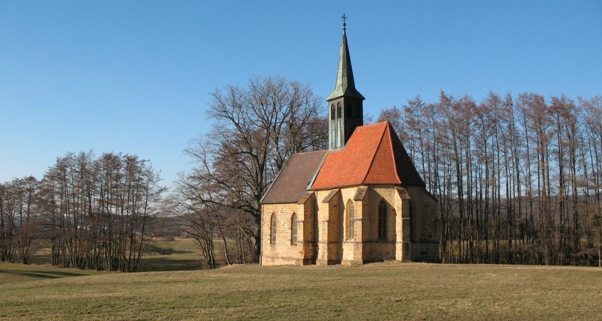 Die St.-Laurentius-Kapelle steht auf einer grünen Wiese, umgeben von kahlen Bäumen, unter einem klaren blauen Himmel., © Landkreis Göppingen Die St.-Laurentius-Kapelle steht auf einer grünen Wiese, umgeben von kahlen Bäumen, unter einem klaren blauen Himmel., © Landkreis Göppingen