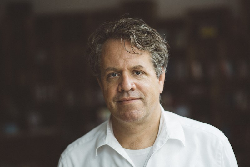 Ein Mann in einem weißen Hemd steht vor einem unscharfen Hintergrund und blickt in die Kamera., © Kulturhaus Schwanen Ein Mann in einem weißen Hemd steht vor einem unscharfen Hintergrund und blickt in die Kamera., © Kulturhaus Schwanen